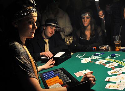 Croupier im 20er Jahre Outfit spielt Blackjack mit den verkleideten Gästen.