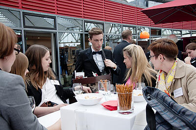 Bauchladenjungen rätselt mit Gästen auf einer Kundenveranstaltung Bauchladenjungen rätselt am Tisch mit Gästen auf einer Kundenveranstaltung