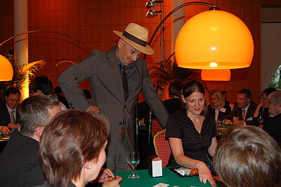 Schauspieler als Walk Act beim Firmenjubiläum der Simcorp GmbH Schauspieler schaut Croupier beim Blackjack über die Schulter und guckt skeptisch.